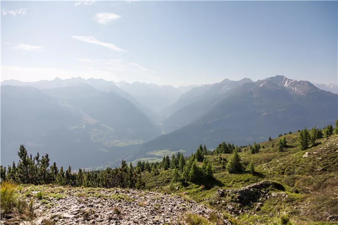 Eine beeindruckende Berglandschaft mit sanften Hügeln und einem klaren Himmel. Im Hintergrund sind die majestätischen Berge zu sehen.