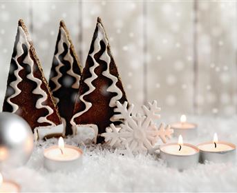 Drei festliche Tannenbaum-Kekse stehen auf einem Bett aus Schnee. Kerzen und eine Schneeflocke ergänzen die winterliche Dekoration.