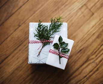 Zwei schön verpackte Geschenke auf einem Holztisch. Die Geschenke sind mit Naturmaterialien dekoriert, darunter kleine Zweige.