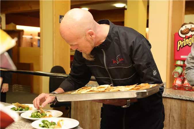 A chef carefully prepares plates with dishes. He holds a tray of food in his hand and focuses on the presentation.