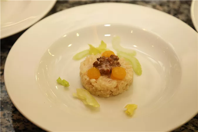 An artistically arranged plate with rice, decorated with mirabelles and a small piece of meat. Some leaves of lettuce complement the dish.