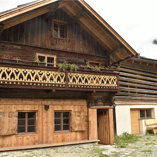 Ein traditionelles Holzhaus mit einem liebevoll verzierten Balkon. Der Garten ist mit Sitzecken ausgestattet und umgeben von grüner Natur.