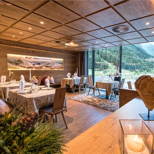 Ein elegantes Restaurant mit Holzmöbeln und schön eingedeckten Tischen. Große Fenster bieten einen Blick auf die umliegende Berglandschaft.