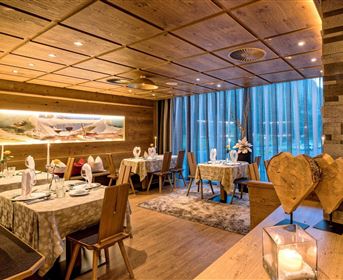 An elegant restaurant with wooden interiors and warm lighting. The table decoration is tasteful and inviting, overlooking large windows.
