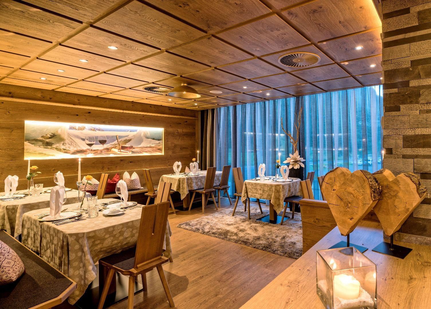 Ein elegantes Restaurant mit Holzelementen und stilvollen Tischen. Große Fenster bieten viel Licht und einen einladenden Blick auf die Umgebung.