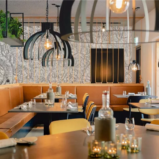 Ein modernes Restaurant mit stilvollen Lampen und gemütlichen Sitzecken. Die warme Farbgebung und die kreative Wandgestaltung schaffen eine einladende Atmosphäre.