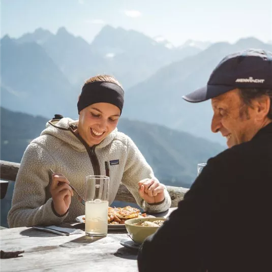 A cheerful atmosphere while dining in the mountains. In the background, majestic mountains and a clear sky can be seen.