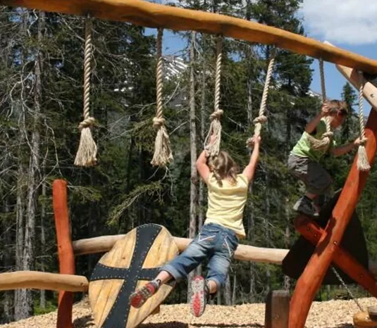 A playground in nature with a wooden swing and climbing elements. Children play and enjoy the fresh air among the trees.