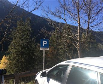 Ein Parkplatzschild steht in der Natur. Im Hintergrund sind Bäume und Berge sichtbar.