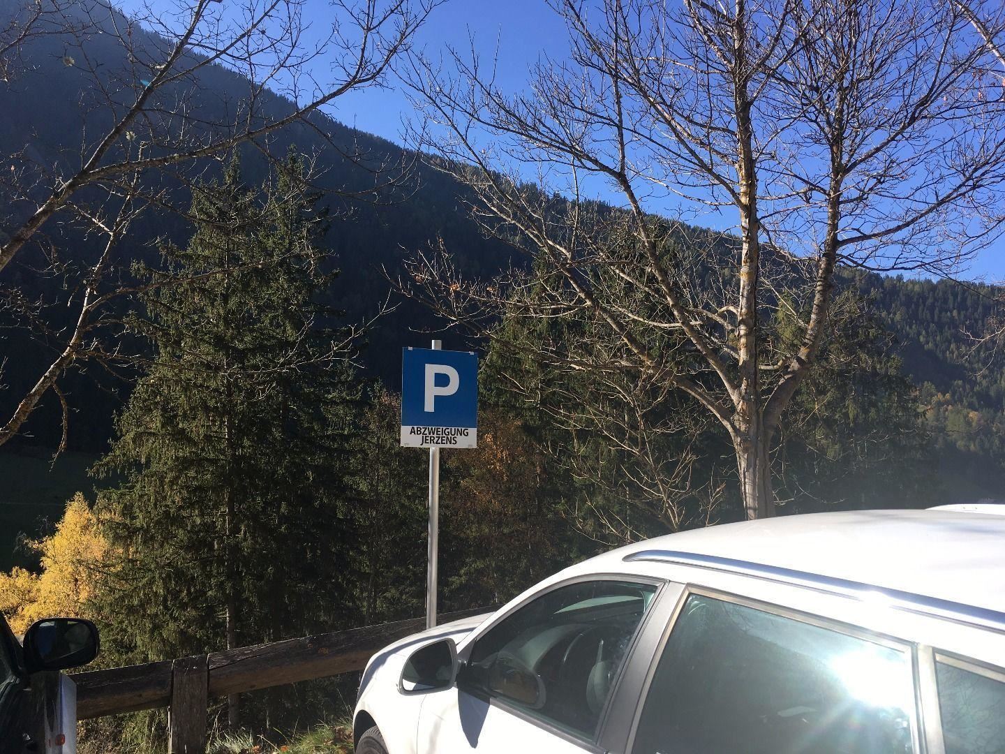 Ein Parkplatzschild steht in der Natur. Im Hintergrund sind Bäume und Berge sichtbar.