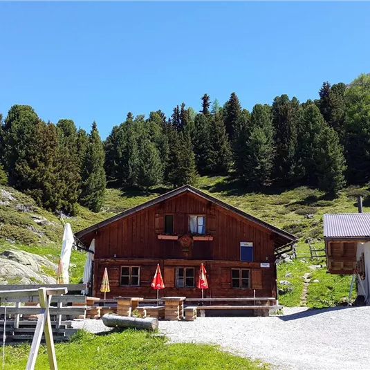 A cozy mountain cabin with a wooden facade and red umbrellas. Surrounded by green trees and a picturesque landscape.