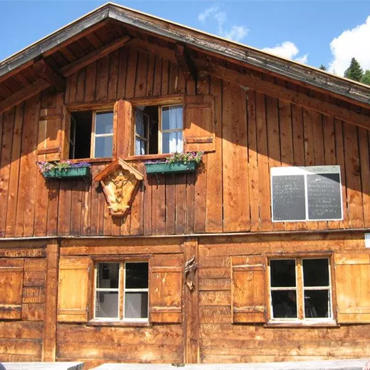 Ein rustikales Holzhaus mit einem traditionalen Design. Die Fenster sind mit Blumenkästen geschmückt, und die Fassade zeigt natürliche Holzfarbe.
