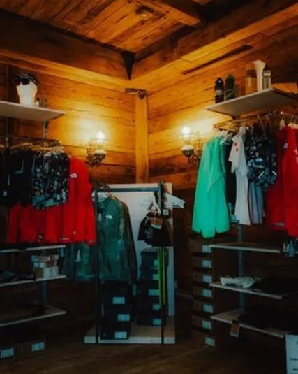 Ein gemütlicher Laden mit Holzregalen, die Kleidung aufbewahren. Die Wände sind aus Holz und die Beleuchtung ist warm und einladend.