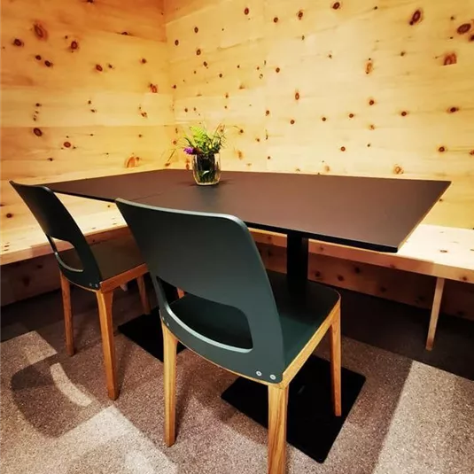 A minimalist room with a black table and two green chairs. On the table is a small vase with flowers.