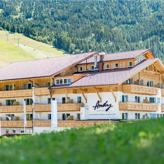 Ein modernes Hotel im alpinen Stil umgeben von Bergen. Die Fassade zeigt Holzverkleidung und große Fenster.