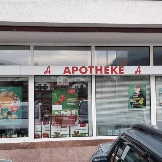 Eine Apotheke mit einem großen Schaufenster, das verschiedene Gesundheitsprodukte zeigt. Die Fenster sind hell und einladend gestaltet.