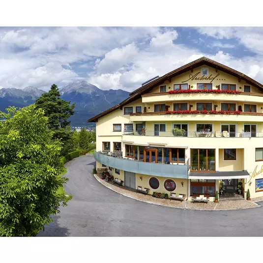 Ein modernes Hotelgebäude in malerischer Umgebung. Im Hintergrund sind Berge und ein bewölkter Himmel zu sehen.