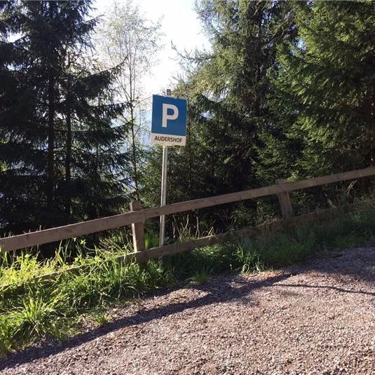 A parking sign stands in front of a wooded landscape. The surroundings are green and sunny.
