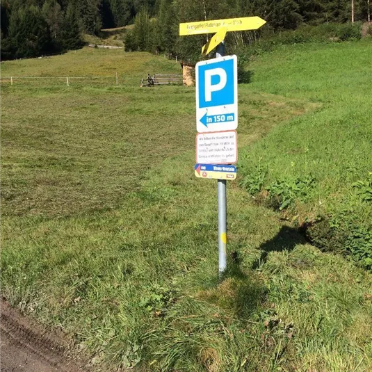 A park sign on a meadow. In the background, there are trees and a beautiful blue sky.
