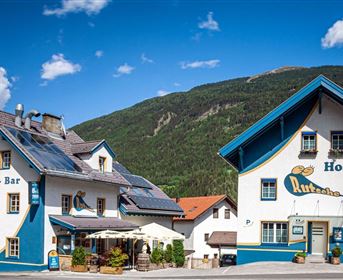 Ein buntes Hostel mit einem Pub und einer Bar in einer malerischen Berglandschaft. Die Gebäude sind freundlich gestaltet und laden zum Verweilen ein.