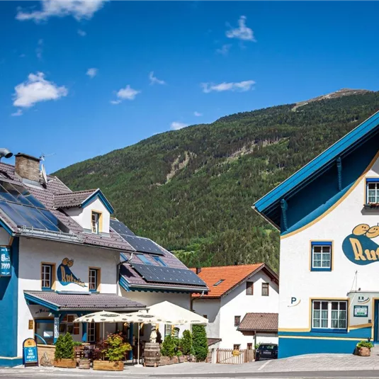 Ein buntes Hostel mit einem Pub und einer Bar in einer malerischen Berglandschaft. Die Gebäude sind freundlich gestaltet und laden zum Verweilen ein.