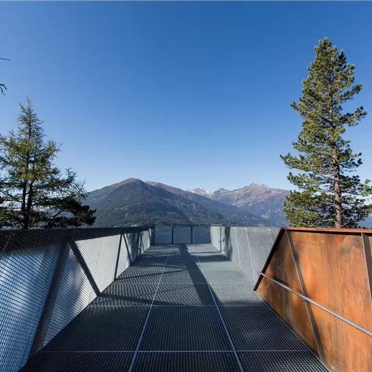 Eine Aussichtsplattform mit Blick auf Berge und Bäume. Der Himmel ist klar und blau.