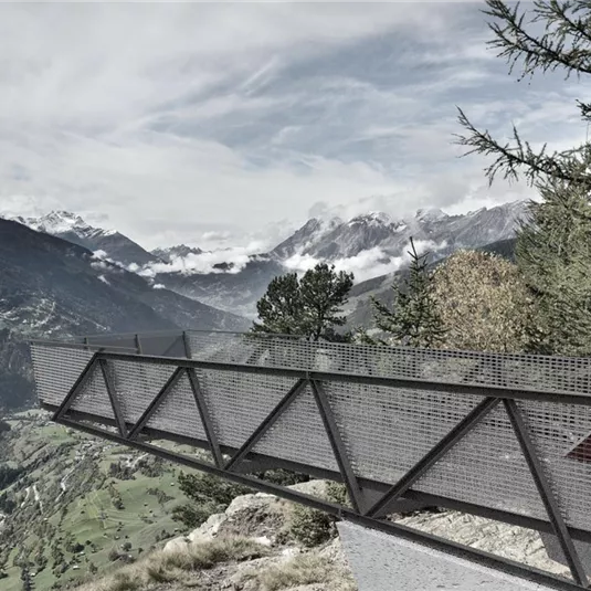 Eine moderne Aussichtsplattform mit Blick auf Berge und Täler. Die Wolken hängen tief über der Landschaft.