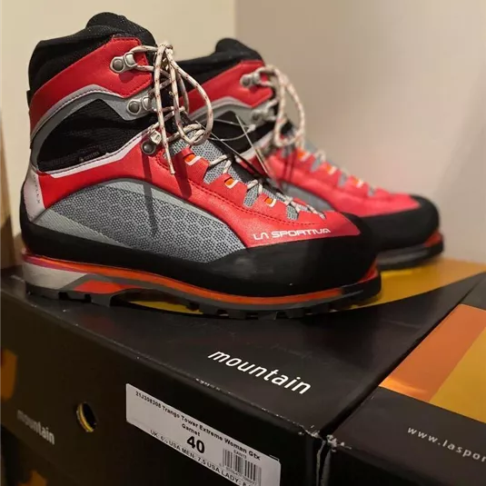 Ein Paar rote Bergschuhe mit grauen und schwarzen Details steht auf einer Schuhbox. Die Schuhe sind für Outdoor-Aktivitäten konzipiert.