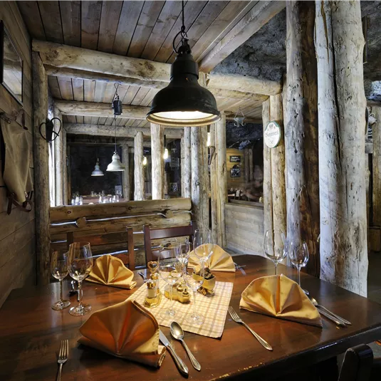 A rustic restaurant with wooden walls and a cozy atmosphere. The table is set for a meal with elegant napkins and glasses.