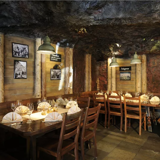A cozy restaurant with wooden furniture and a rustic, cave-like atmosphere. The walls are designed with stone and wood, complemented by warm lighting.