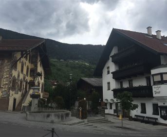 Ein malerisches Dorf mit traditionellen Häusern und einer schönen Berglandschaft im Hintergrund. Der Himmel ist bewölkt, was der Szenerie eine ruhige Atmosphäre verleiht.