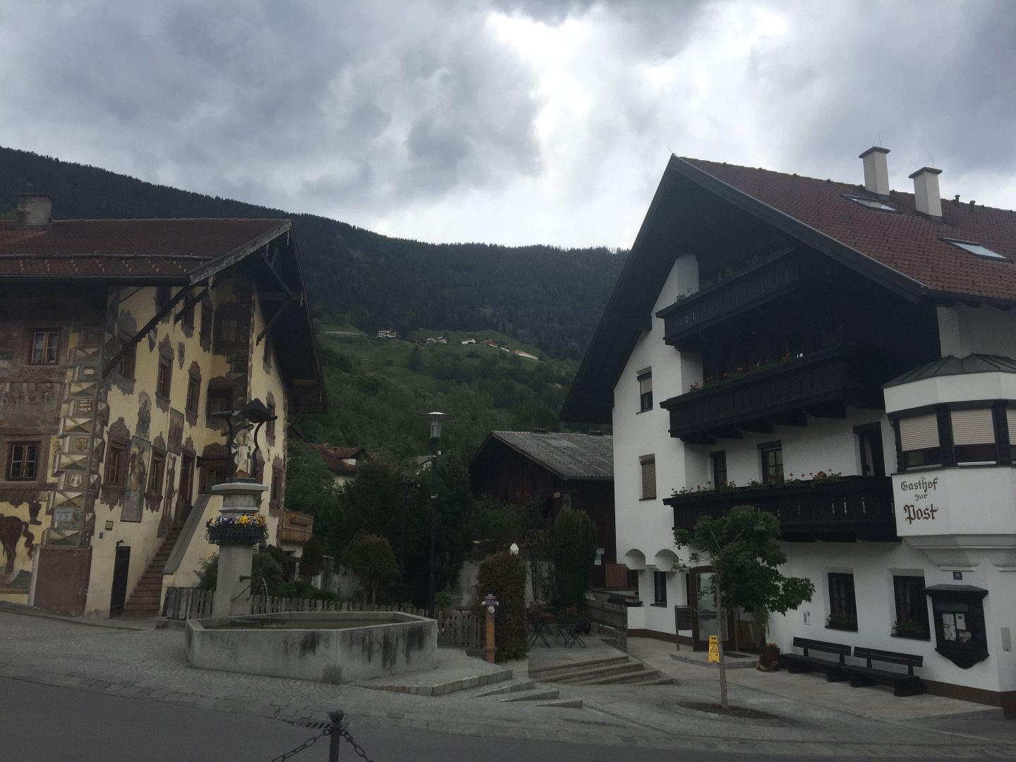 Ein malerisches Dorf mit traditionellen Häusern und einer schönen Berglandschaft im Hintergrund. Der Himmel ist bewölkt, was der Szenerie eine ruhige Atmosphäre verleiht.