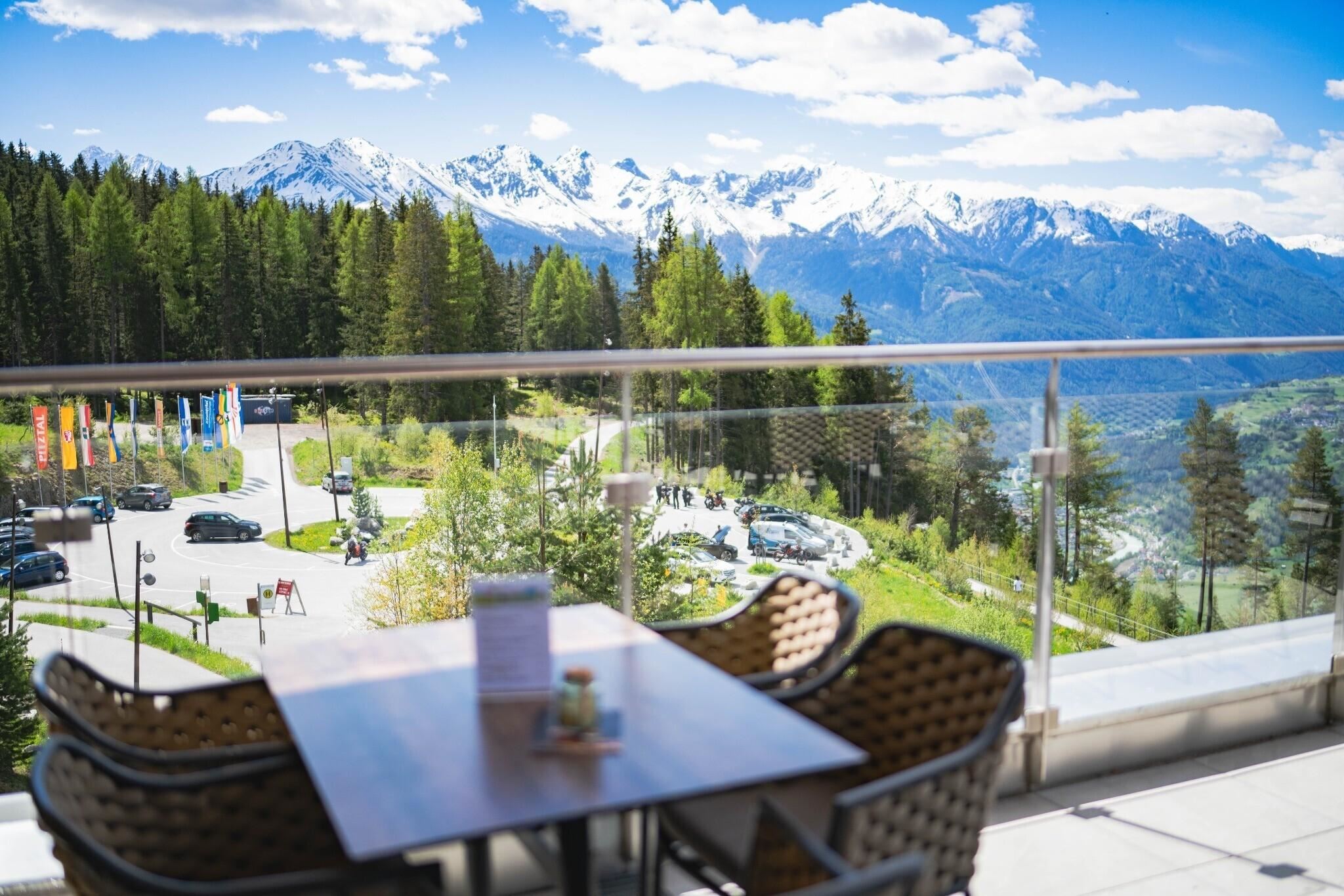 Ein schöner Ausblick auf die Berge mit schneebedeckten Gipfeln und einer grünen Landschaft darunter. Auf der Terrasse stehen Stühle und ein Tisch, ideal für eine entspannte Pause.