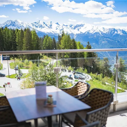 Ein schöner Ausblick auf die Berge mit schneebedeckten Gipfeln und einer grünen Landschaft darunter. Auf der Terrasse stehen Stühle und ein Tisch, ideal für eine entspannte Pause.