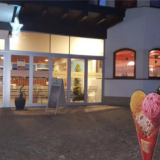 An ice cream parlor with large windows and warm light. In front of the entrance stands an ice cream umbrella with two scoops of ice cream.