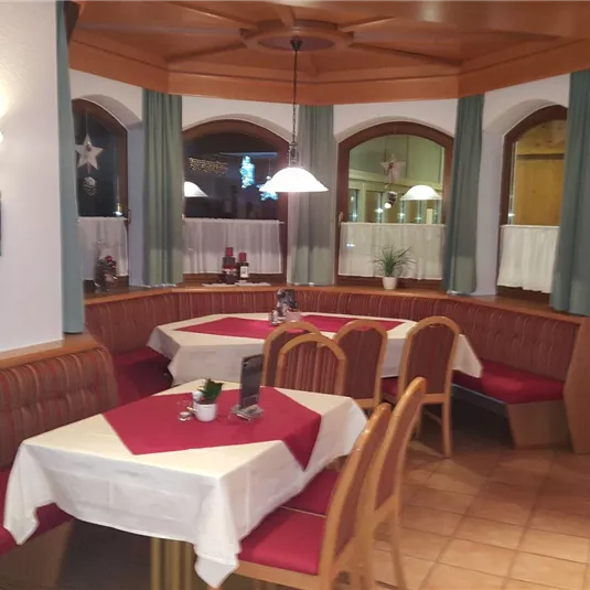 A cozy restaurant with seating and red-and-white checkered tablecloths. The walls are decorated in warm colors, and large windows let in light.