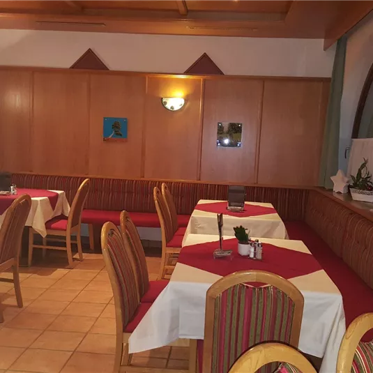 A cozy restaurant with wooden furniture and tablecloths in shades of red and beige. The walls are decorated with pictures, the light is warm and inviting.