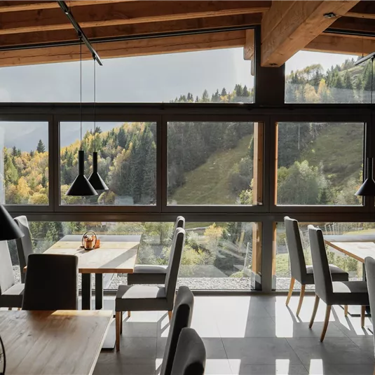 A modern restaurant with wooden decor and large windows. The view of the colorful nature in the background is impressive.