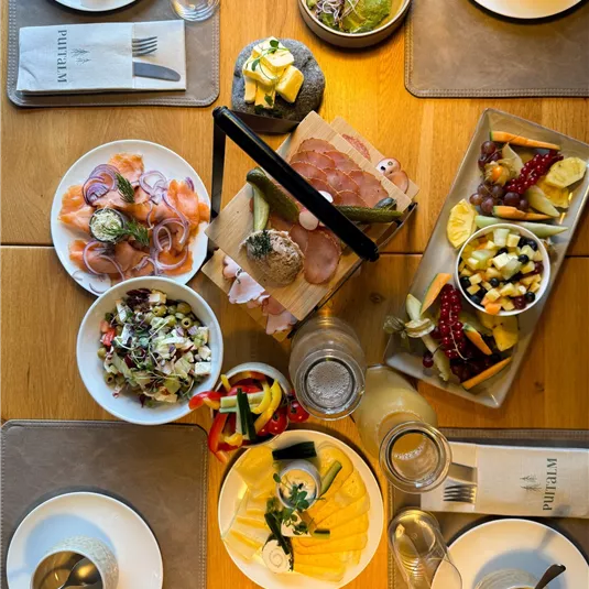 A table with various delicious dishes, including salads, cold cuts, and fresh fruits. The atmosphere is inviting and sociable.