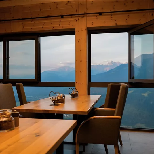 A cozy dining room with wooden tables and chairs. Large windows offer an impressive view of the mountains.