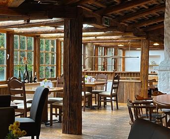 Ein gemütliches Restaurant mit Holzmöbeln und großen Fenstern. Es gibt eine warme Atmosphäre und Blick auf die Natur.