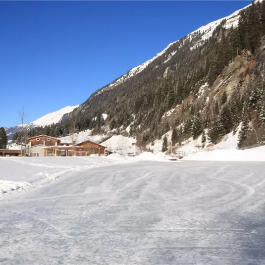 Eine schneebedeckte Landschaft mit einem gefrorenen See und Bergen im Hintergrund. Die klare, blaue Himmelsfarbe ergänzt die winterliche Szenerie.