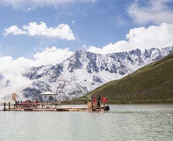Ein schön gelegener Floß auf einem ruhigen See, umgeben von majestätischen, schneebedeckten Bergen. Der Himmel ist klar mit einigen Wolken.