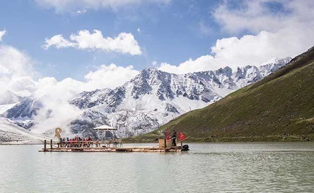 Ein schön gelegener Floß auf einem ruhigen See, umgeben von majestätischen, schneebedeckten Bergen. Der Himmel ist klar mit einigen Wolken.