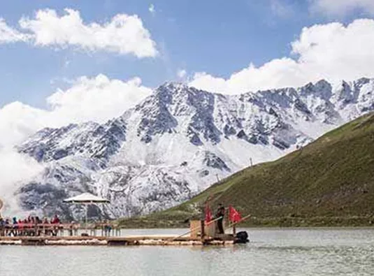 Ein schön gelegener Floß auf einem ruhigen See, umgeben von majestätischen, schneebedeckten Bergen. Der Himmel ist klar mit einigen Wolken.