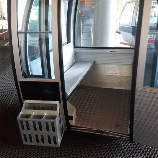 Eine Seilbahn mit einer leeren Kabine und einem Abfallbehälter daneben. Der Boden ist rutschfest und eignet sich für den Aufenthalt von Fahrgästen.