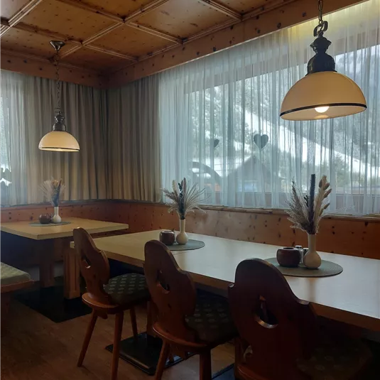 A cozy restaurant with wooden walls and large windows. The tables are nicely decorated with flowers and the lighting creates a warm atmosphere.
