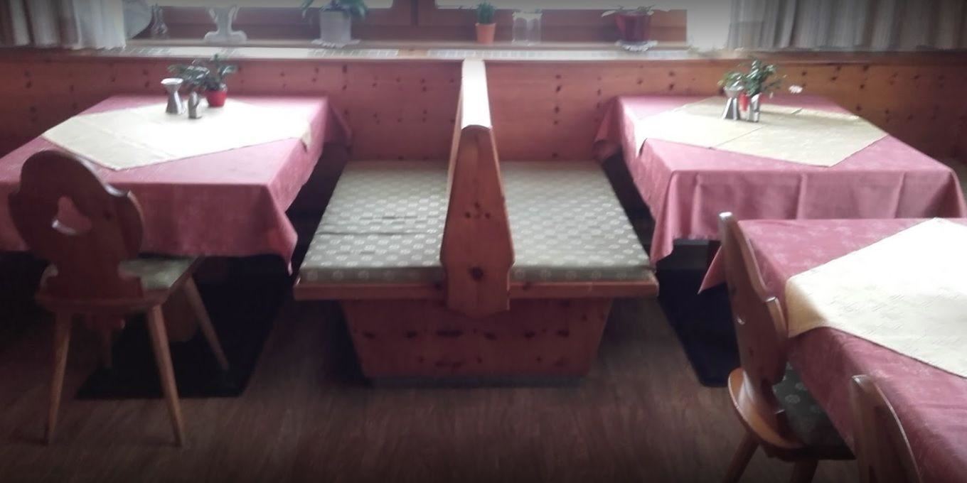 A cozy restaurant with wooden tables and benches. The tables are decorated with pink tablecloths and small plants.