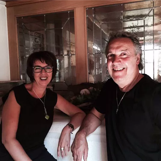 A smiling couple stands together in a cozy room. They seem relaxed and friendly.