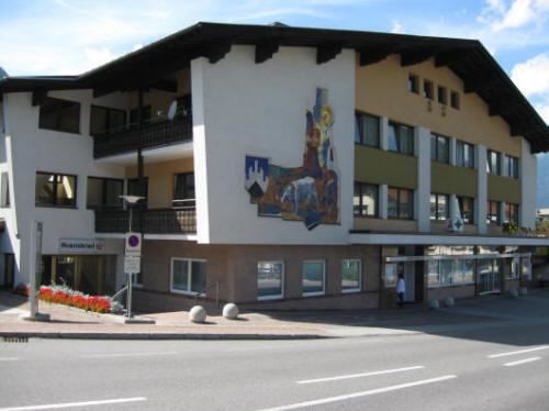 Ein modernes Gebäude mit einem großen Wandbild und Balkonen. Vor dem Gebäude sind Blumenbeete und eine Straßenansicht sichtbar.